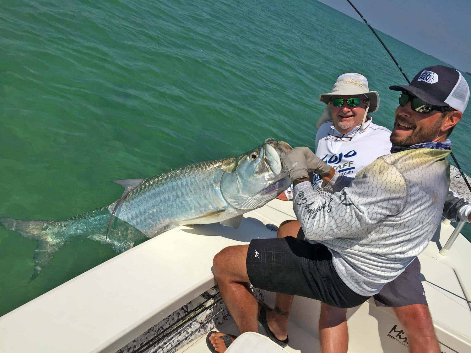 Two men on boat, one wearing MSC Finny Redfish shirt and holding massive fish